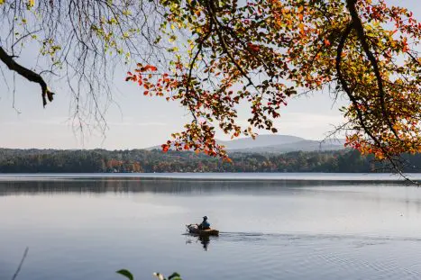 Person in kayak on calm lake with fall foliage