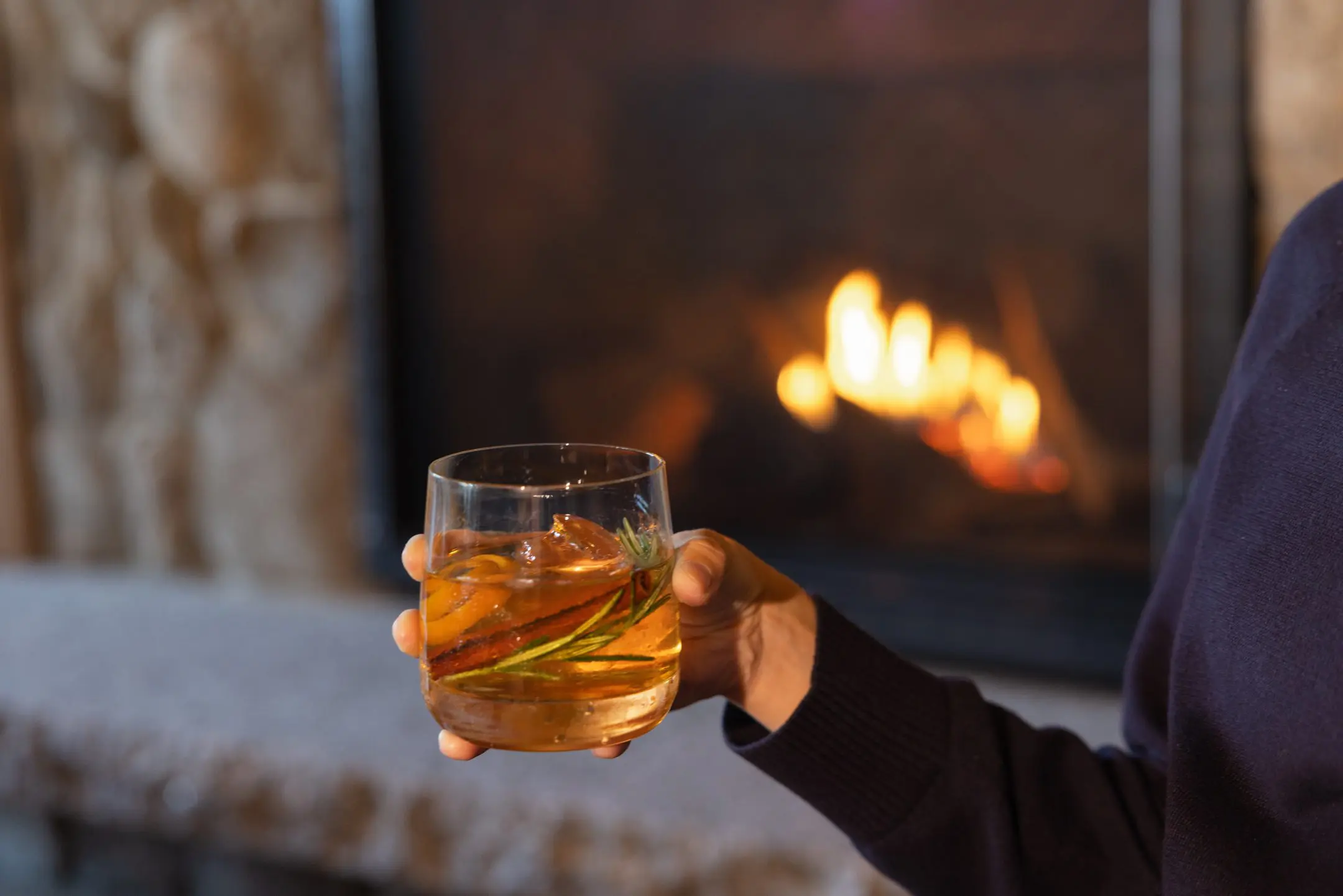 Person holding cocktail by fireplace