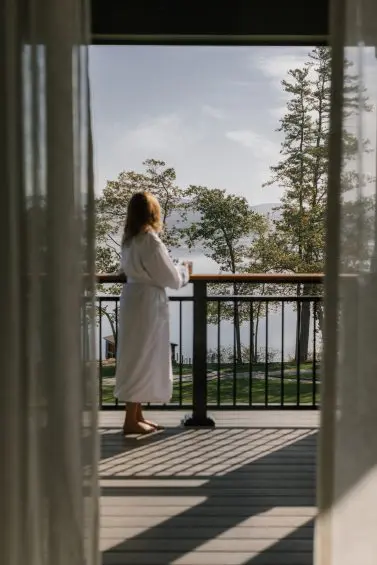 Guest in robe enjoying lake view from private balcony.