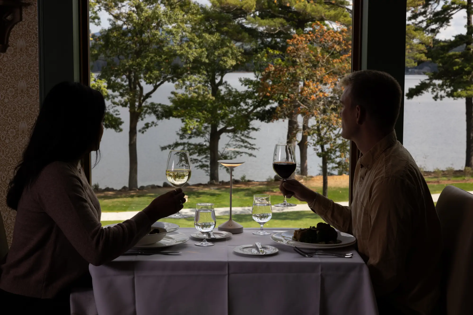 Couple dining with lake view through large window.