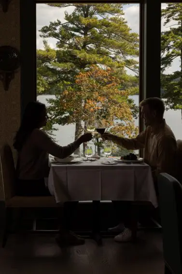 Couple toasting wine in lakeside dining room window view.