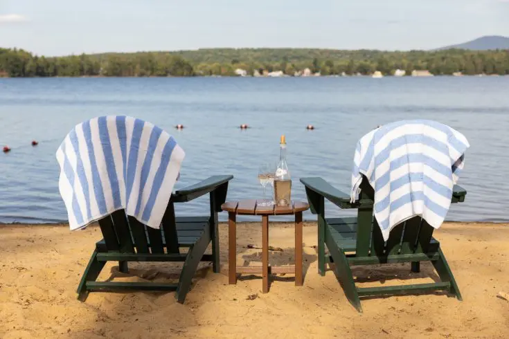Picnic basket and wine beside Adirondack chairs on the sandy beach.