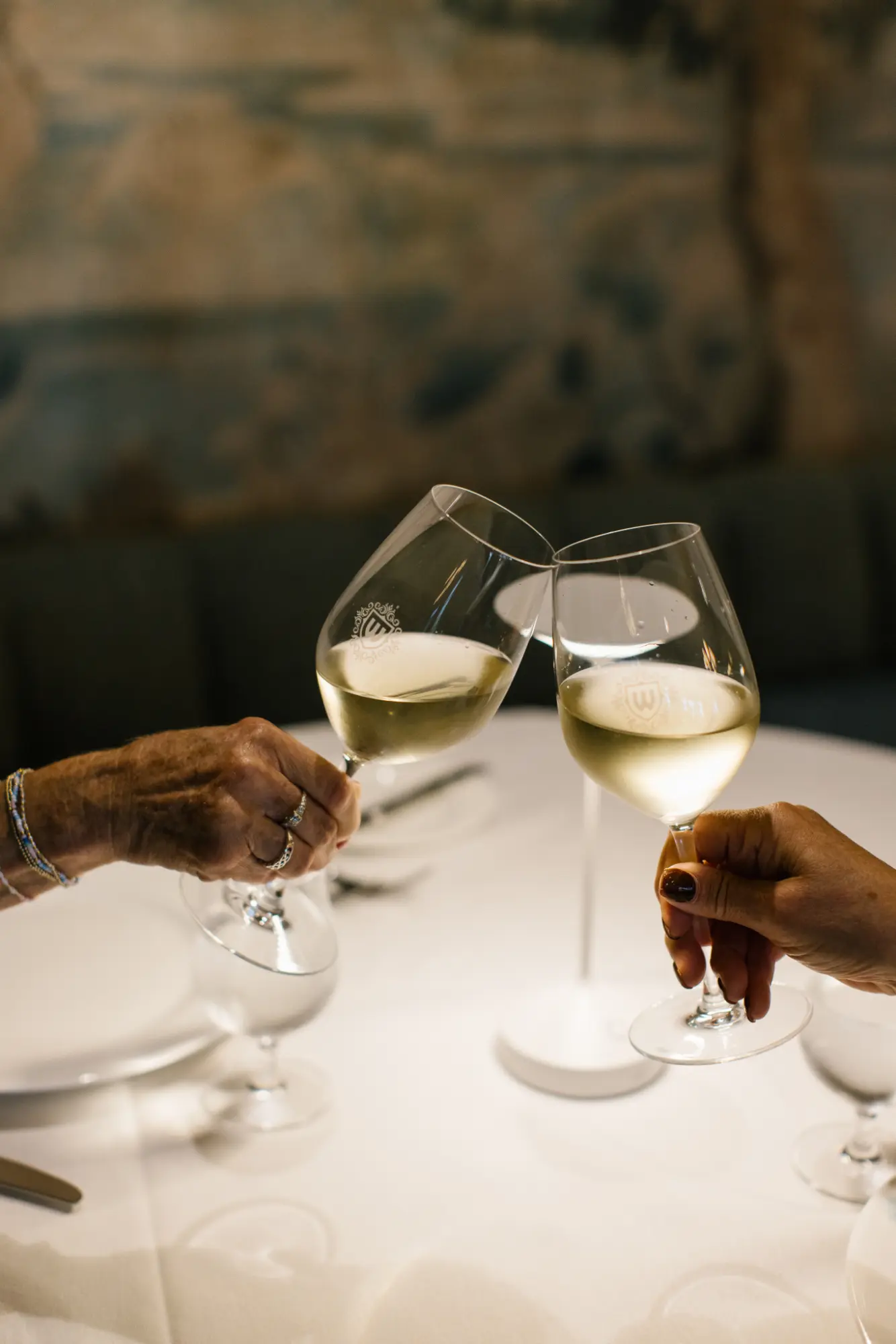Two guests clinking glasses of white wine, celebrating in an elegant dining setting.
