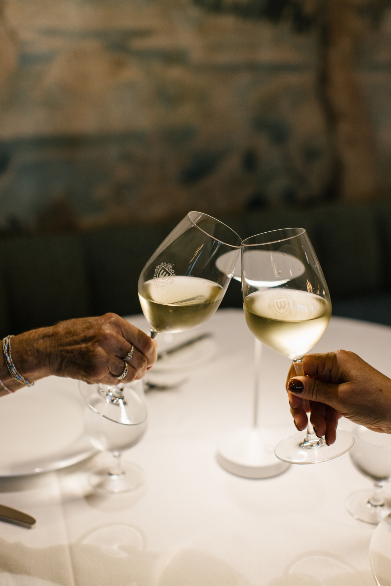 Two guests clinking glasses of white wine, celebrating in an elegant dining setting.
